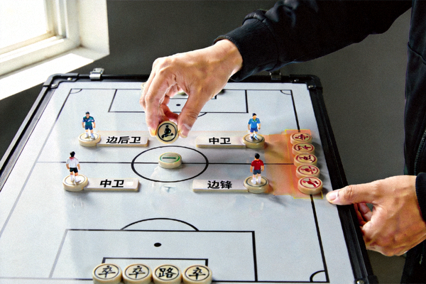教练在战术板上摆放磁力棋子，演示三中卫体系的边路防守站位